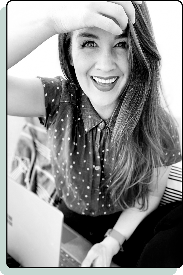 Dani is sitting cross-legged on the floor weather gold pants and a blank tank top. She's holding a silver water tumbler in her left hand and there's a planner sitting on the floor to her right. She has long brown hair and there are various plants sitting on the windowsill in the background.
